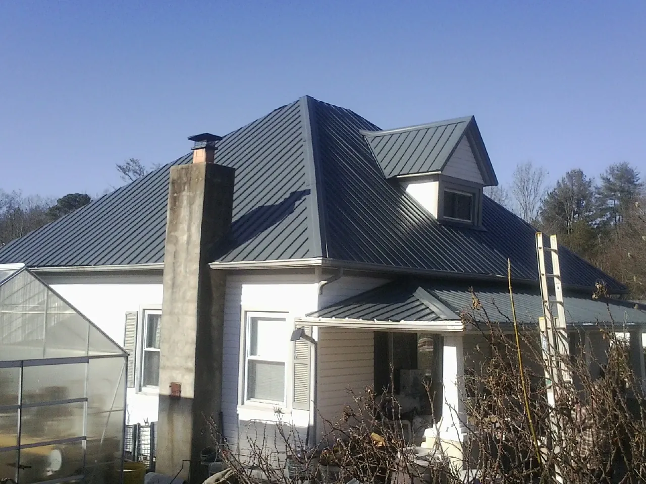 Dark blue standing seam metal roof on a white farmhouse with dormer — Slate & Tile Roof Repair by Roofing Brothers in Breaux Bridge