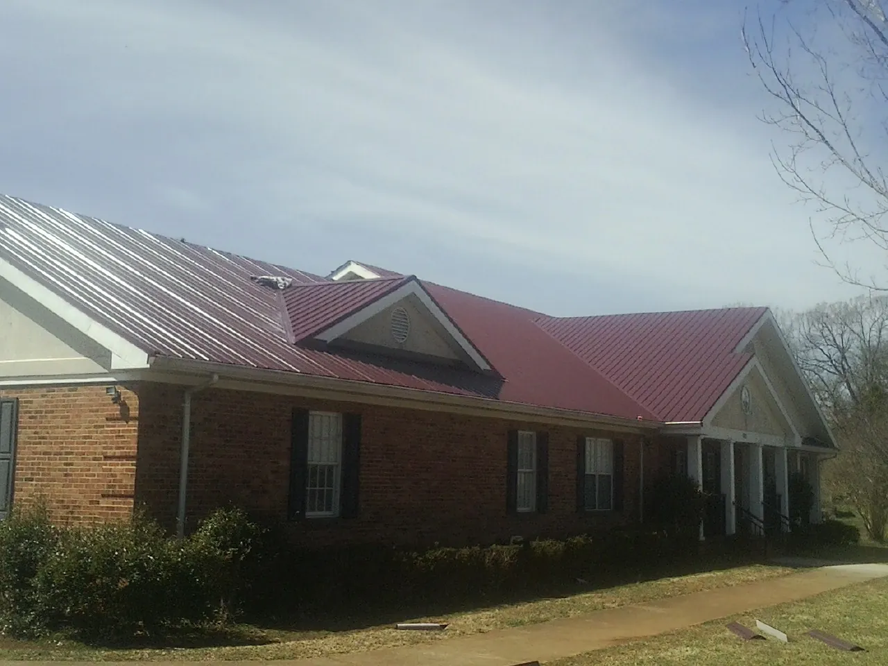 Red metal roof with gabled entries on a long brick building, from a Hail Damage Roof Repair job in Breaux Bridge