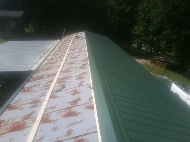 Old rusted panels beside newly installed green metal roofing — Wind Damage Roof Repair by Roofing Brothers in Breaux Bridge