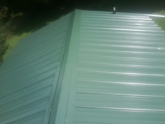 New green metal panels meeting at the ridge of a roof — Flat Roof Repair work by our crew in Breaux Bridge