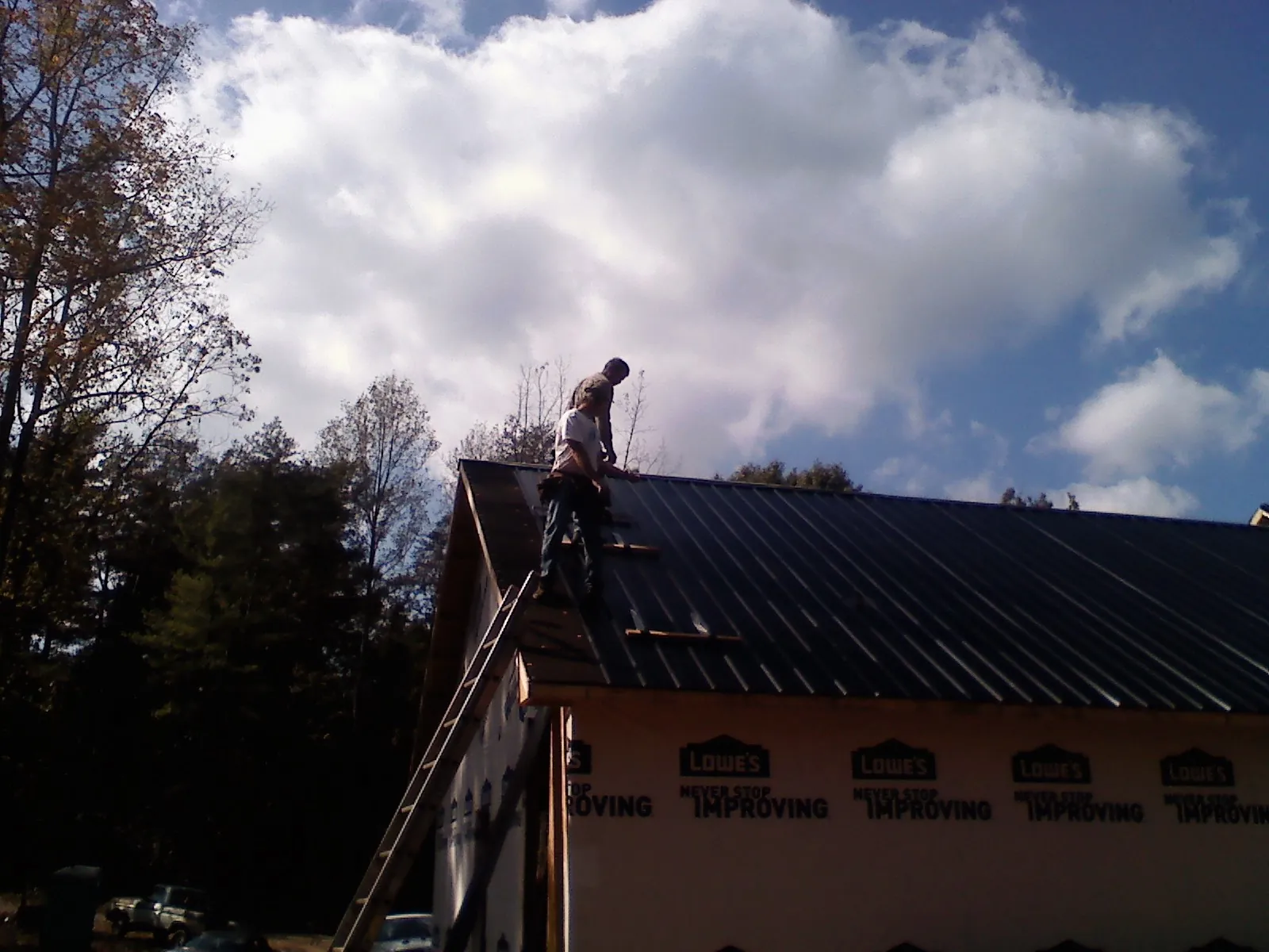 Roofer fastening dark metal panels high against a cloudy sky, from a Roof Inspection job in Breaux Bridge