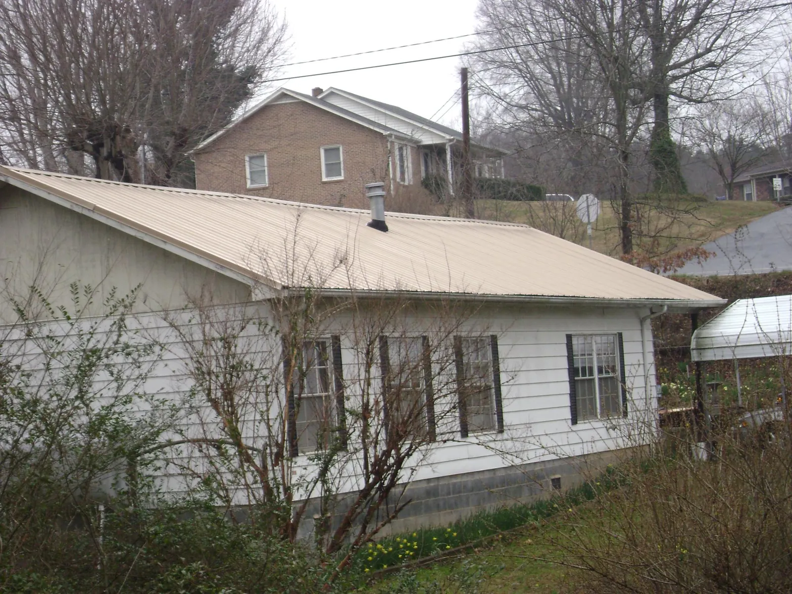 Tan metal roof on a white sided house set into a hillside — Commercial Roofing by Roofing Brothers in Breaux Bridge