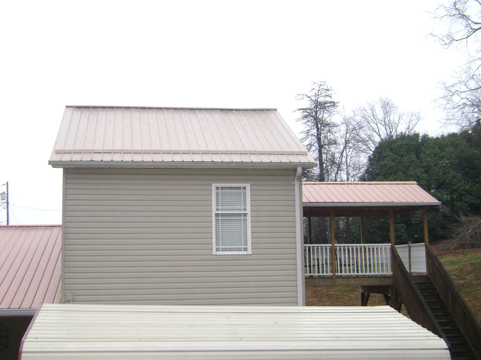 Tan metal roofs on a two story addition and attached porch, from a Roof Replacement job in Breaux Bridge