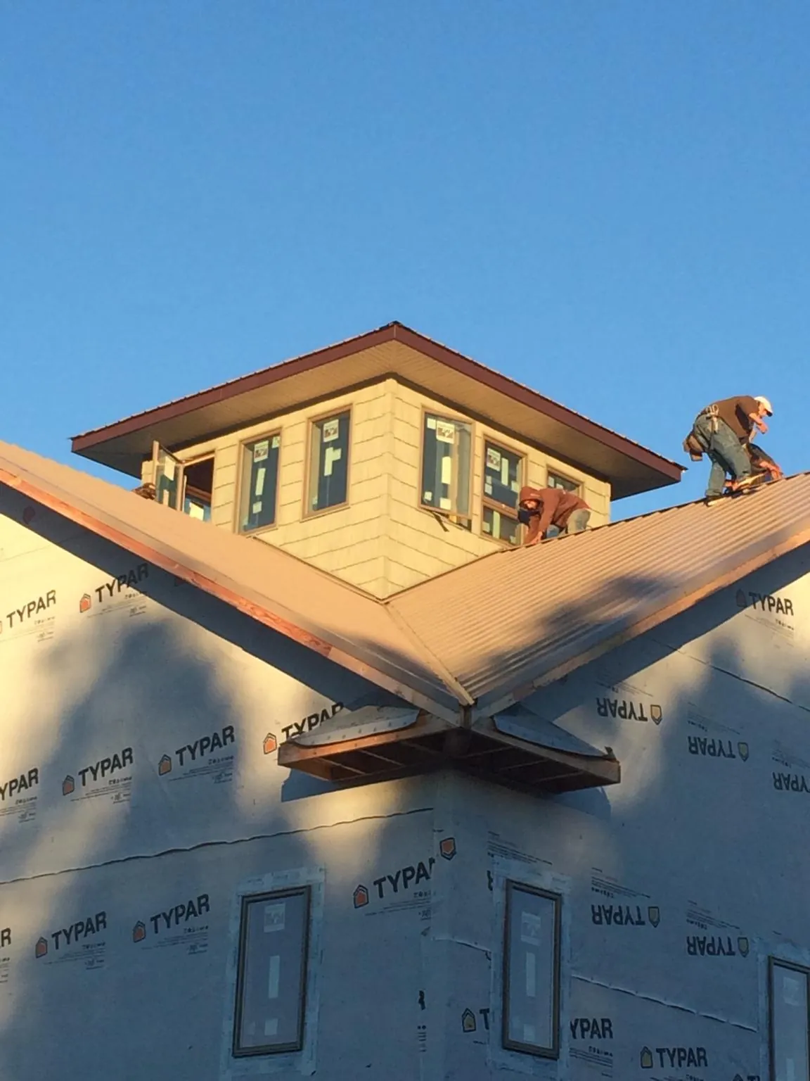 Roofers working around a rooftop cupola on a new metal roof at sunset — Roof Waterproofing in Breaux Bridge by Roofing Brothers